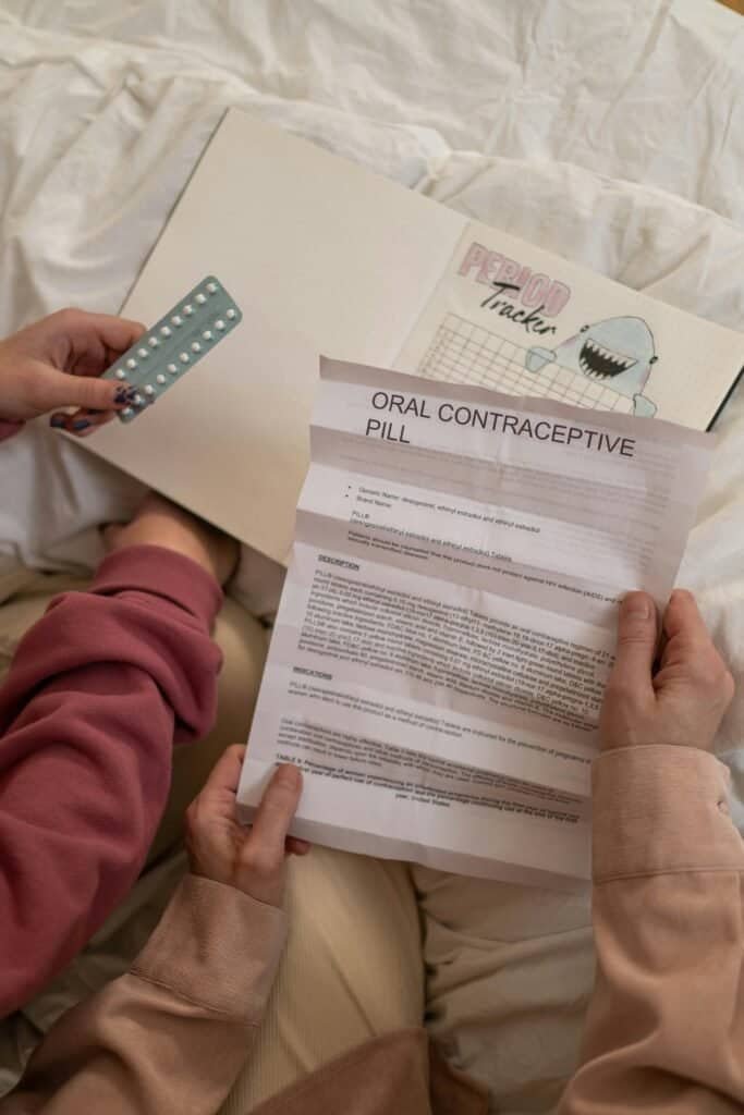 Hands holding oral contraceptive pill leaflet next to period tracker, representing questions about contraceptives